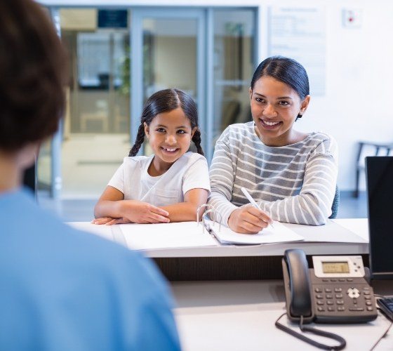 Woman and her child talking to dental team member at front desk