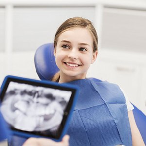 Young girl smiling while dentist reviews X-ray