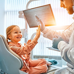 Dentist high-fiving little girl in treatment chair
