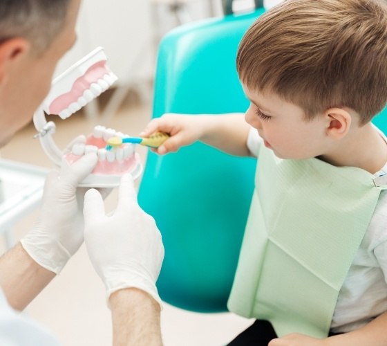 Young boy brushing model of teeth with pediatric dentist