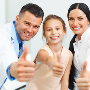 Two dentists and a young girl giving their thumbs up 