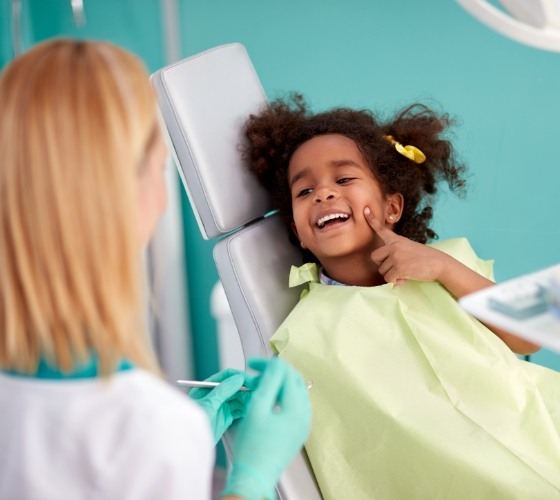 Young girl pointing to her smile while visiting pediatric emergency dentist