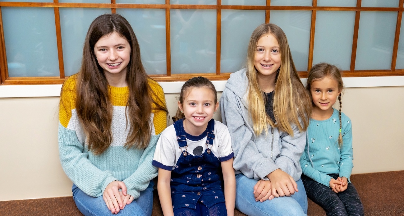 Four smiling kids sitting on bench in pediatric dental office