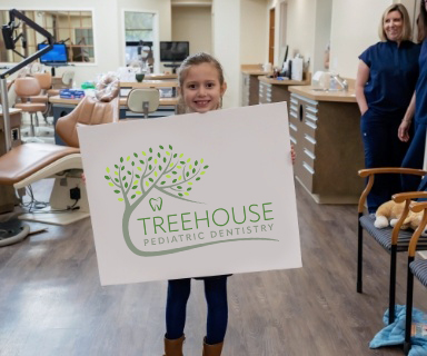 Young girl holding Treehouse Pediatric Dentistry sign