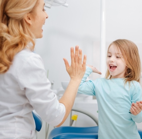 Pediatric dentist giving high five to young girl in dental treatment room