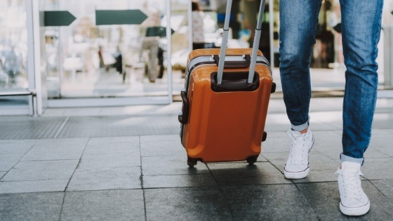 Person carrying a rolling suitcase behind them