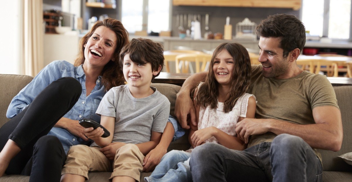 Family of four smiling on couch after pediatric dental services