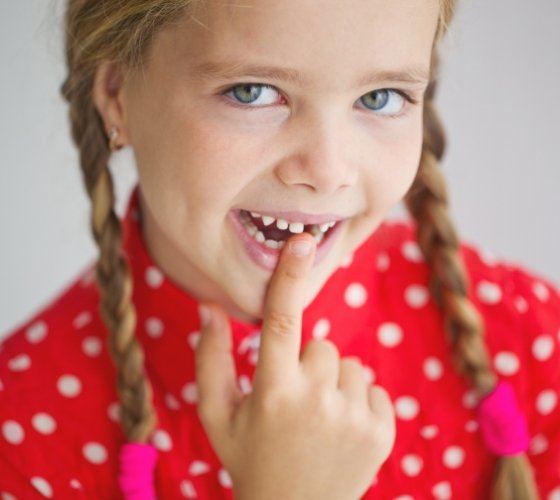 Young girl pointing to gap in smile from missing tooth